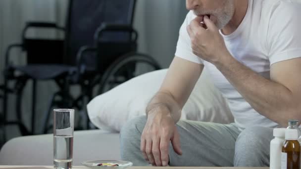 Homme âgé prenant la pilule, regardant fauteuil roulant debout à l'arrière-plan, traumatisme — Video