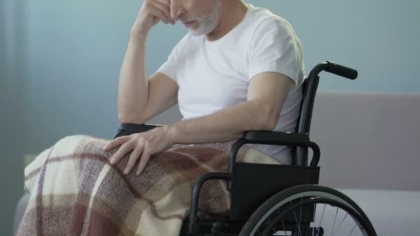 Самотній старший чоловік, сидячи в інвалідному візку в центрі догляду, чекає на родичів — стокове відео