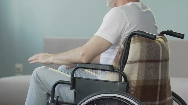 Hombre anciano sentado en silla de ruedas mirando las piernas y asintiendo, perdió la capacidad de caminar — Vídeos de Stock