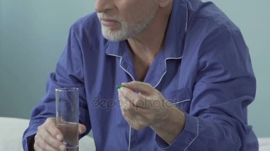 Yaşlı erkek holding hap bir elinde bardak su ağır iç geçiriyorum, başka bir