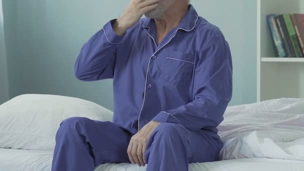 Hombre mayor sentado en el borde de la cama después de levantarse, estirándose y sonriendo — Vídeos de Stock