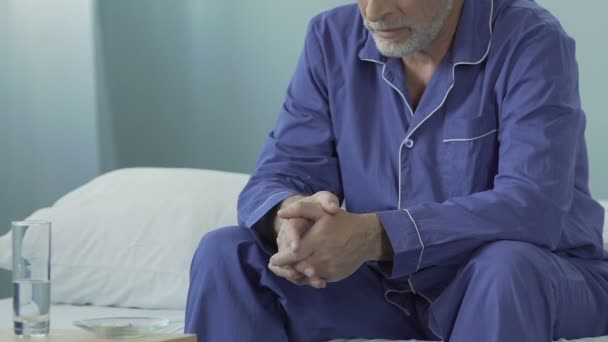Старий сидить у піжамі на ліжку з таблетками в мисці на нічному столі, пригнічений — стокове відео