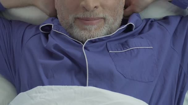 Alter Mann liegt im Bett und dehnt sich, zufriedener Mann wacht auf, Nahaufnahme von oben — Stockvideo