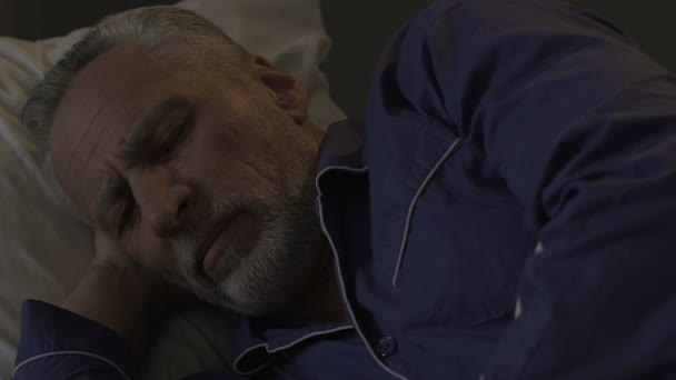 Бородатый старый мужчина лежит в постели бодрствуя, не в состоянии заснуть ночью бессонница — стоковое видео