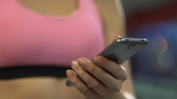 Активная женщина прокручивает экран смартфона в тренажерном зале, используя спортивное мобильное приложение — стоковое видео