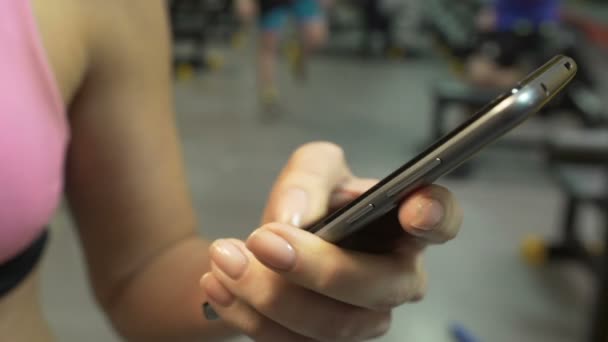 Jovencita en busca de información sobre el teléfono inteligente en el gimnasio, aplicación de fitness desplazamiento — Vídeos de Stock