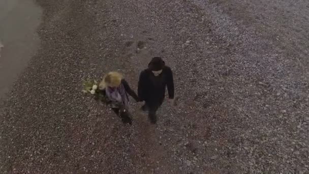 Giovane coppia che si tiene per mano mentre cammina in riva al mare, donna con fiori, amore — Video Stock