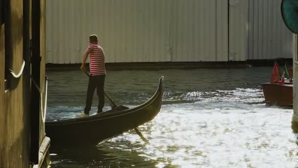 Převozník stojící na gondole a veslování kanálem se sluníčko odráží na něm