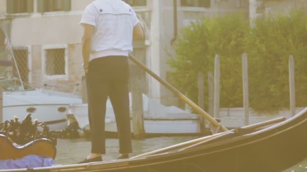 Гондольє стоїть на кормі і веслує на човні ліниво, жестикулюючи, маючи розмову — стокове відео