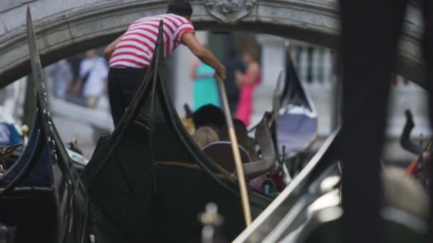 Line of gondolas trying to pass under low arched bridge, boats moored sideways — Stock Video