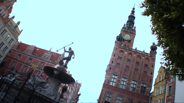 Fuente con estatua de Neptuno frente al edificio con torre del reloj en Gdansk — Vídeos de Stock