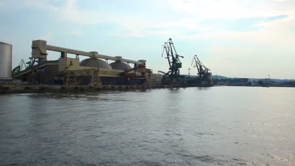 Båt går sjövägen, närmar sig wharf med enorma bodar och kranar i hamn — Stockvideo