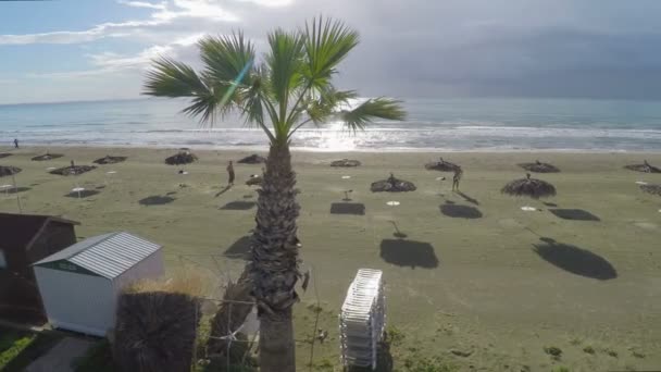 Двоє чоловіків, сонячні ванни на пляжі з солом'яними парасольками, відпочинок в Ларнаці — стокове відео