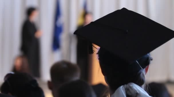Жінка з білим бантом у волоссі в академічній сукні дивиться на сцену, освіта — стокове відео