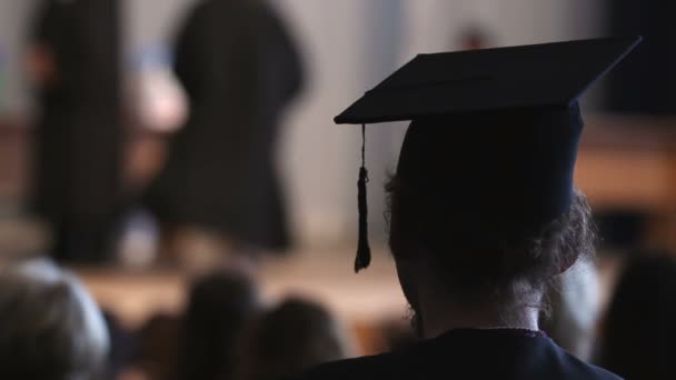 Lockigt hårman i mortarboard och akademiska klä tittar på scenen, examen — Stockvideo