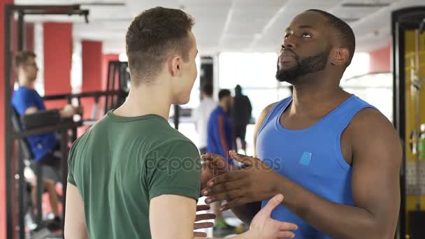 Due allenatori di nazionalità diverse che discutono sul tempo di allenamento in palestra — Video Stock