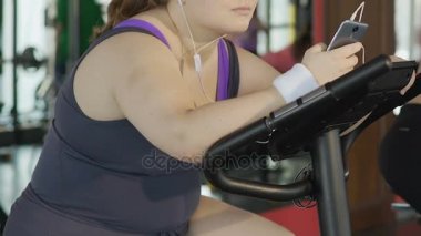 Halsiz sıkılmış Bayan iplik egzersiz bisikleti pedal, smartphone, tembel oynarken