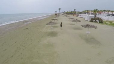 Uzun saçlı erkek vurdu hızlı sahil şeridi üzerinde hasır plaj şemsiyeleri, hava arasında çalışan