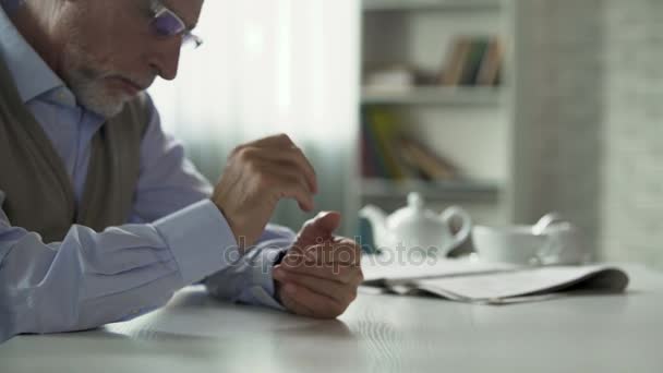 Podeszłym wieku mężczyzna siedzący przy stole i zacierając ręce, zdejmując okulary, martwi — Wideo stockowe