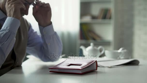 Pensionista masculino colocando óculos, abrindo álbum de fotos na mesa, memórias antigas — Vídeo de Stock