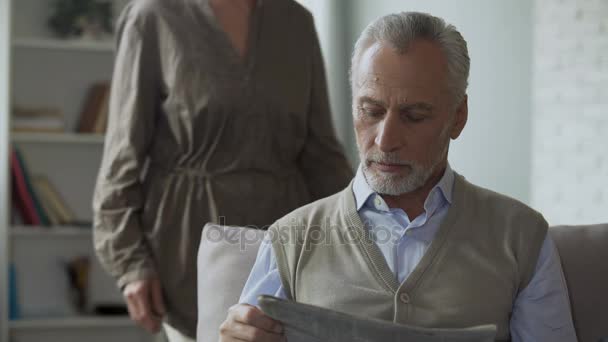 Senior mannen läser tidningen, kvinna kommer bakifrån att krama, familj morgon — Stockvideo