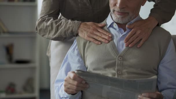 Manlig pensionär läsa tidningen, kvinnliga kramar bakifrån, kärleksfull ömhet — Stockvideo