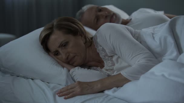 Пожилая пара лежит в постели бодрствуя, женщина повернулась спиной к мужчине, обида — стоковое видео