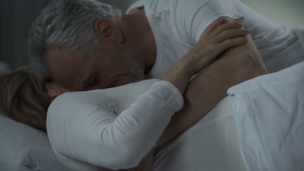 Старшая пара обнимает и ласкает в постели, мужчина целует женщину шею, влечение — стоковое видео