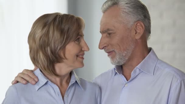 Feliz pareja de ancianos mirándose y sonriendo a la cámara, publicidad — Vídeo de stock