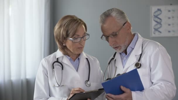 Опытные врачи-мужчины и женщины сравнивают результаты, консультируют по диагностике — стоковое видео