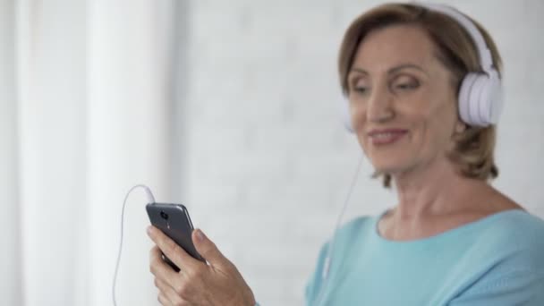 Női nyugdíjas fejhallgató hallgat a mobiltelefon a dalt, és a tánc — Stock videók
