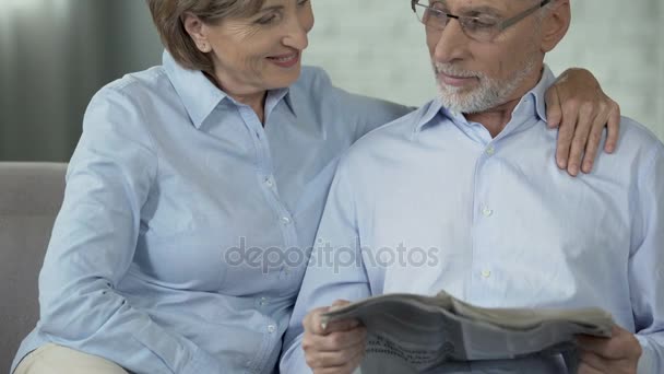 Mujer jubilada abrazando marido que está leyendo el periódico, feliz pareja de ancianos — Vídeo de stock