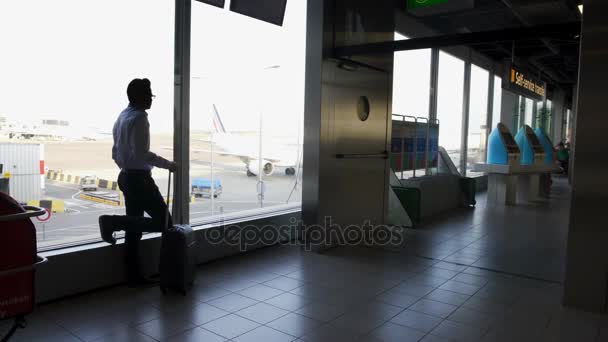 Задумчивый мужчина с чемоданом ждет посадки и смотрит в окно — стоковое видео