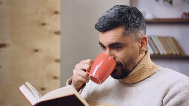 Bärtiger Mann liest interessantes Buch und trinkt Tee oder Kaffee, Freizeit — Stockvideo