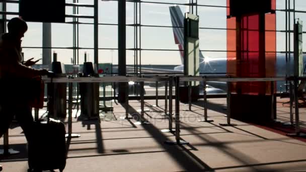 Maleta rodante femenina en la terminal del aeropuerto, con teléfono móvil, viajando al extranjero — Vídeo de stock