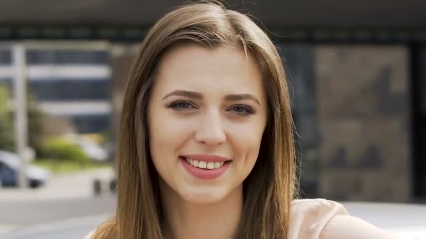 Молодая успешная женщина регулирует волосы улыбаясь и глядя в камеру, лицо крупным планом — стоковое видео