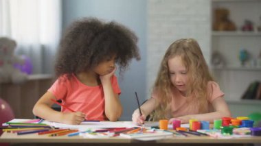 Genç çok ırklı kadın masada oturan ve renkli kalemler ile çizim