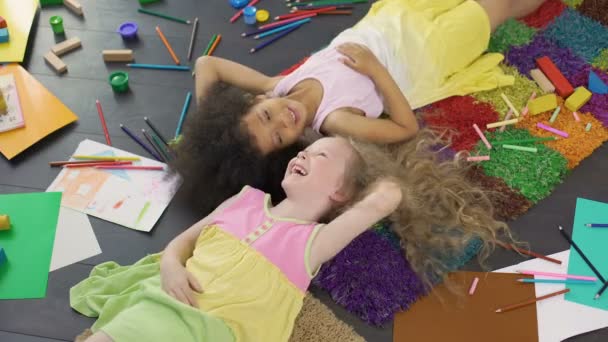 Dos niñas multirraciales tumbadas en la alfombra y riendo, feliz infancia — Vídeos de Stock