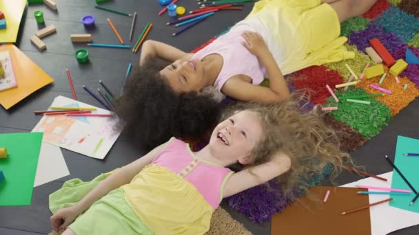 Little multiracial girls lying on the floor, laughing and enjoying holidays — Stock Video