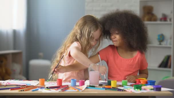 En el jardín de infantes, dos chicas multirraciales positivas pintando con acuarelas, hobby — Vídeo de stock