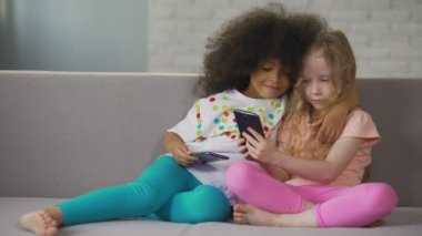 Çok ırklı kız kanepe, sarılma ve alma selfie smartphone üzerinde oturan