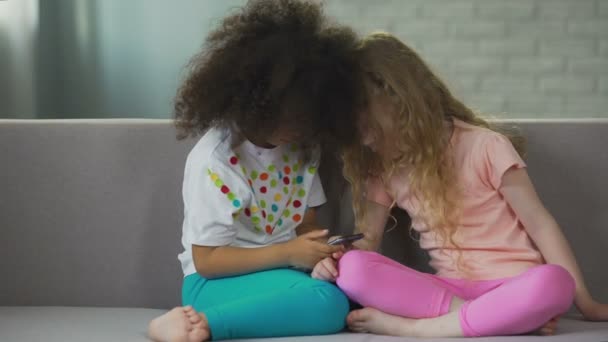 Multiethnische Kinder, die auf der Couch sitzen und auf dem Smartphone spielen, moderne Technik — Stockvideo