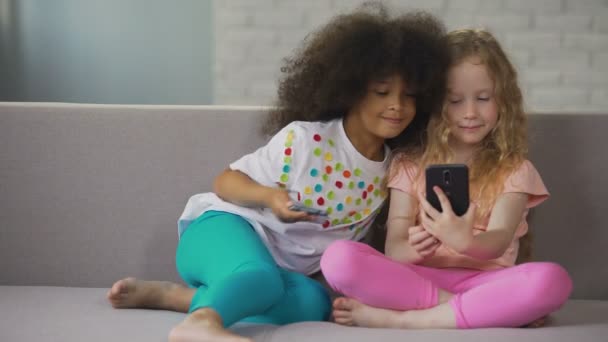 Hermanas multiraciales sentadas en el sofá y tomando selfie en el teléfono inteligente en casa — Vídeos de Stock