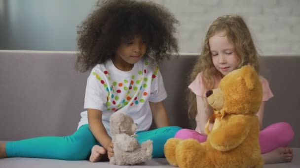 Zwei kleine multirassische Mädchen sitzen auf der Couch und spielen mit Teddybären — Stockvideo