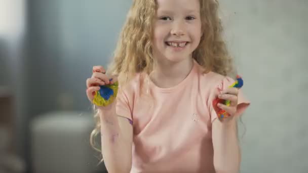 Позитивна дівчина показує розфарбовані долоні в камеру і сміється, щасливе дитинство — стокове відео