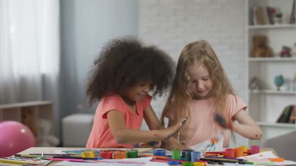 Pequenos amigos multirraciais fazendo impressões coloridas das mãos em papéis, se divertindo — Vídeo de Stock