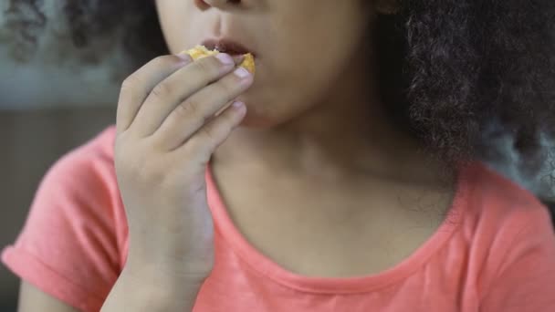 Αστεία σγουρά μαλλιά κορίτσι τρώει cookie στο σπίτι, γκρο πλαν του θηλυκού παιδιού τσιμπολόγημα — Αρχείο Βίντεο