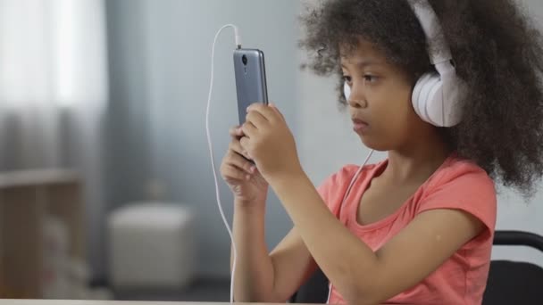 Vážnou afroamerické dítě nosit sluchátka a sledování videa na mobil — Stock video