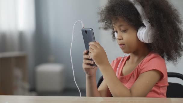 Niño bastante afroamericano usando auriculares y escuchando música en el teléfono celular — Vídeos de Stock