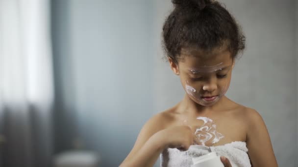 Ragazzina mettendo crema idratante sul corpo e sul viso, copiando il comportamento della madre — Video Stock